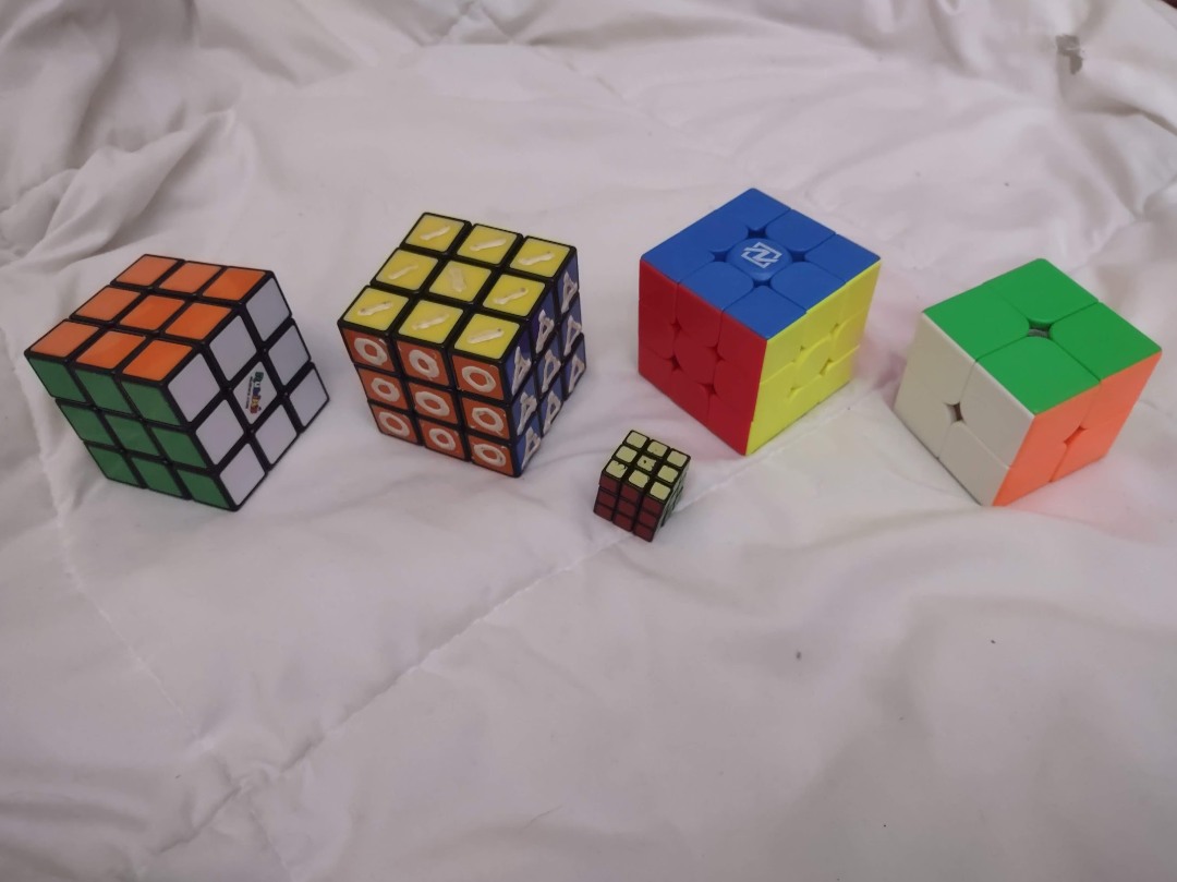 from left to right: a normal rubiks cube, a rubiks cube altered to be solved by touch, a tiny rubiks cube, a speed cube, and a speed 2 by 2 cube.