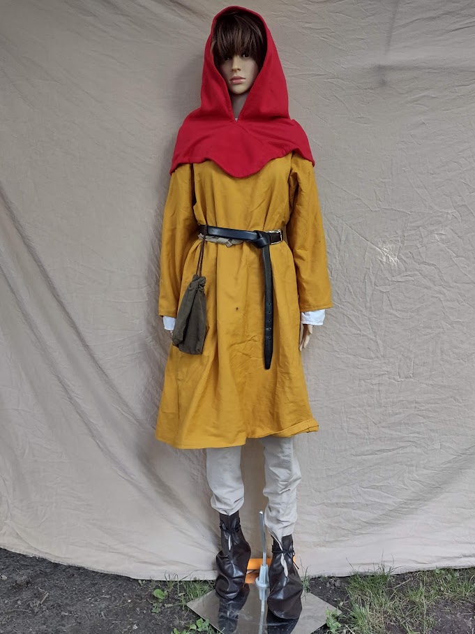 A mannequin wearing a yellow tunic over tan hose and dark brown boots as well as a belt, pouch, and red hood.
