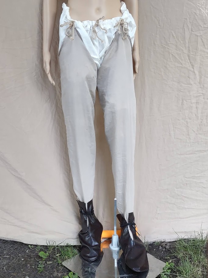 A mannequin wearing white braies, tan hose, and dark brown turn boots.