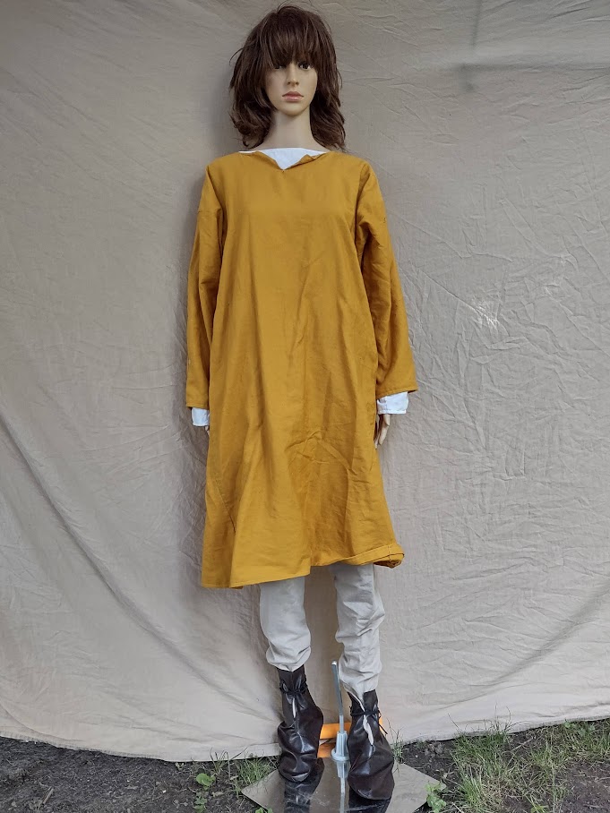 A mannequin wearing a yellow tunic over tan hose and dark brown boots.