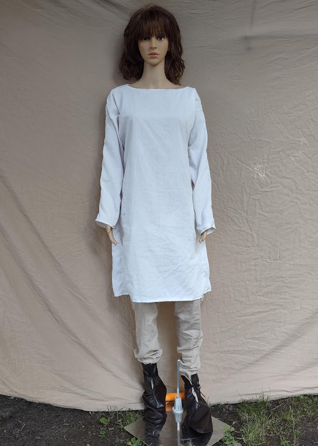 A mannequin wearing a white tunic over tan hose and dark brown boots.